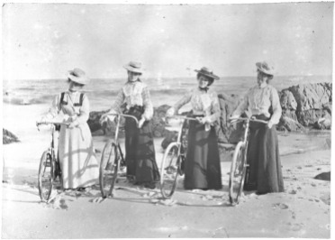 Four women with bicycles on the beach.