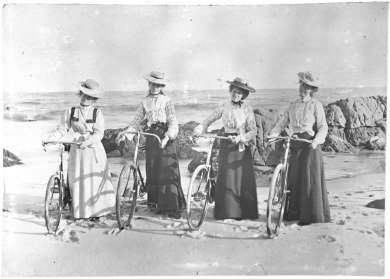 Four women with bicycles on the beach.